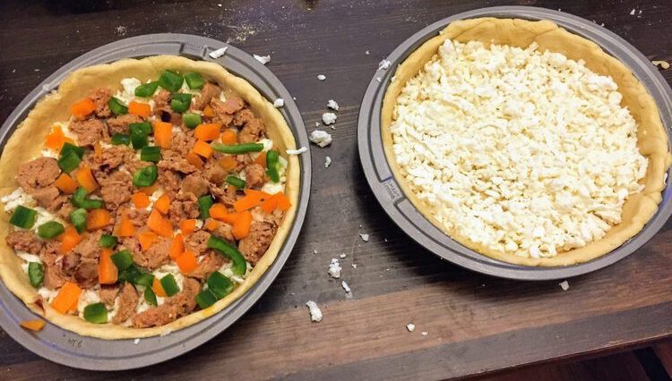 two pans with dough and cheese. One has sausage and peppers in it